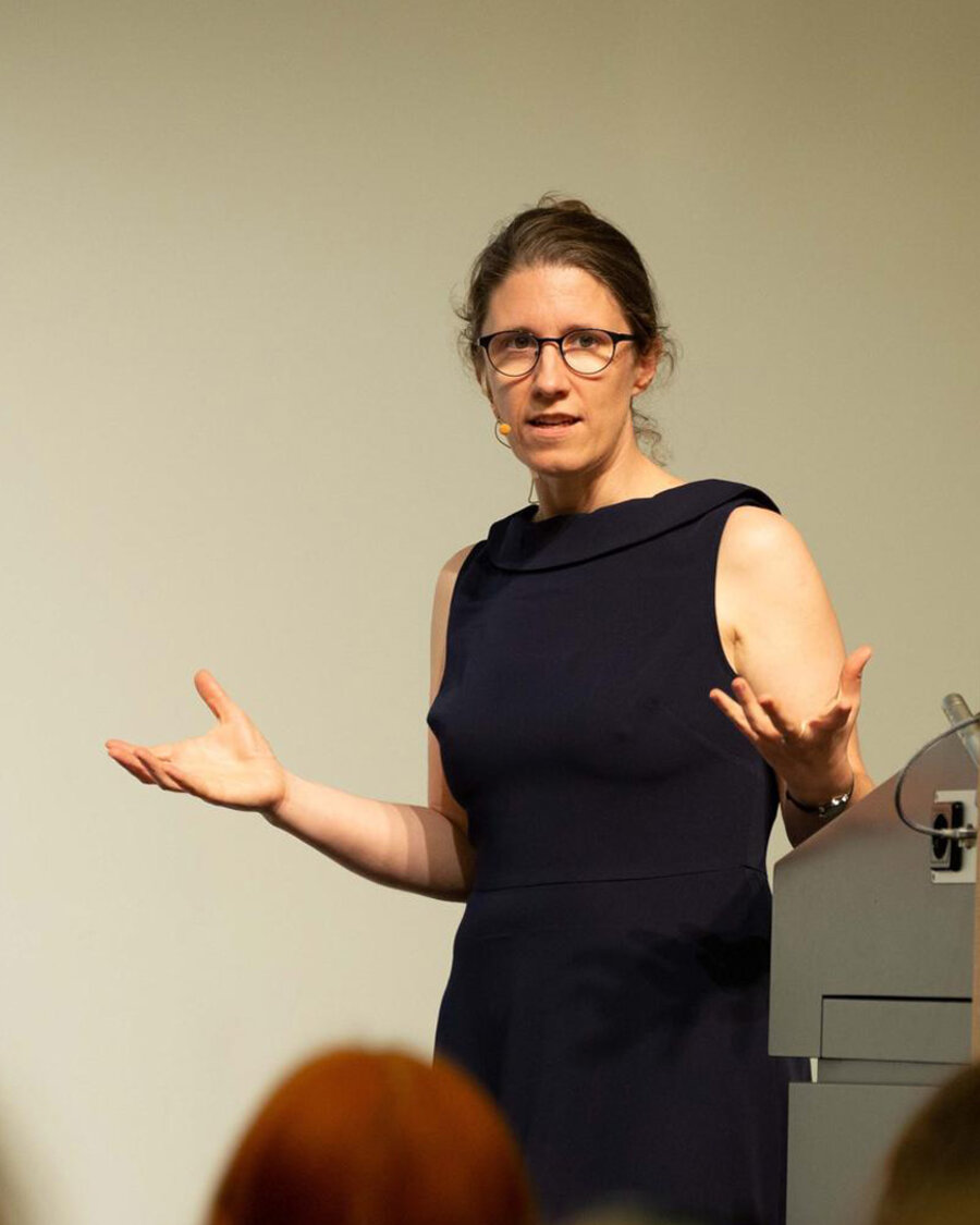 Prof. Dr. Barbara Vetter, Professorin für Theoretische Philosophie an der FU Berlin hält einen Vortrag. Sie trägt ein schwarzes Kleid und gestikuliert in Richtung Publikum, Brain City Berlin.