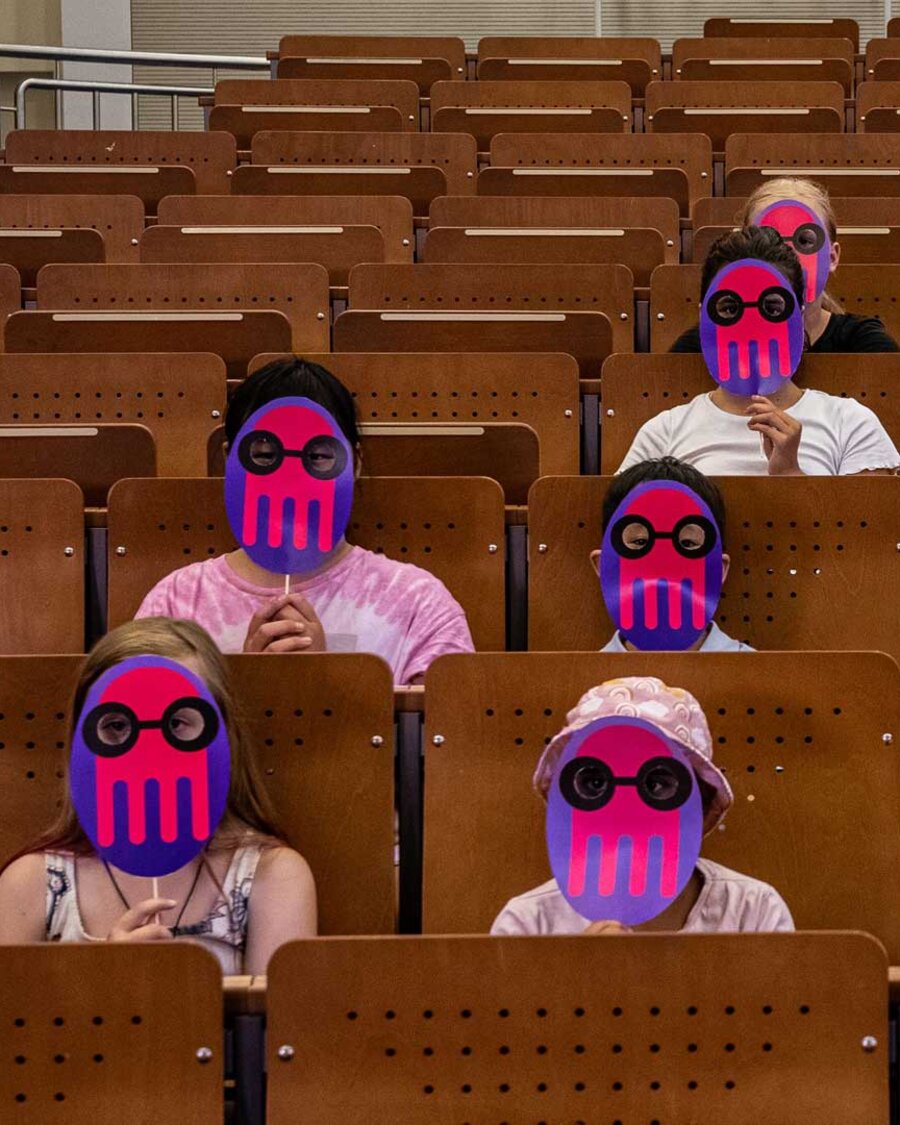 Kinder mit KUL-Masken im Hörsaal.